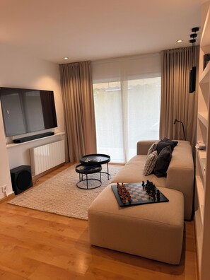 A modern living room with a flat-screen TV, a sofa, a coffee table, and a chessboard. - Luxury Penthouse with Terrace, Pool, and Views (Sant Cugat del Vallès)