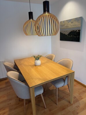 A dining area with a wooden table, grey upholstered chairs, a white vase with a plant, and two pendant lights with a striped design. - Luxury Penthouse with Terrace, Pool, and Views (Sant Cugat del Vallès)