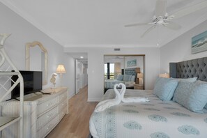 A hotel room with a bed, a television, a dresser, a mirror, and a ceiling fan. - Edgewater Beach Condo 0407 (Destin)