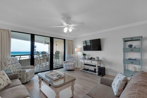 Ein Wohnzimmer mit Glastür zum Balkon, Deckenventilator, Flachbildfernseher und Bücherregal.