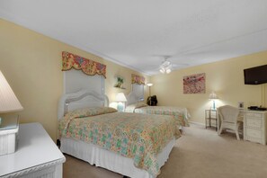Ein Schlafzimmer mit zwei Betten, einem Deckenventilator, einem Fernseher und einem Schreibtisch mit Lampe.