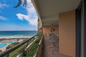 Ein Balkon mit Blick auf Strand und Pool, ein Deckenventilator und Gartenmöbel.