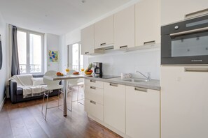 Eine moderne Küche mit weißen Schränken, einem eingebauten Ofen und einem Essbereich mit grauem Sofa und weißen Stühlen.