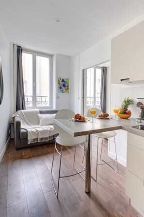 Eine moderne Küche mit Essbereich, ausgestattet mit einem grauen Sofa, weißen Stühlen, einem Holztisch und einer Obstschale.