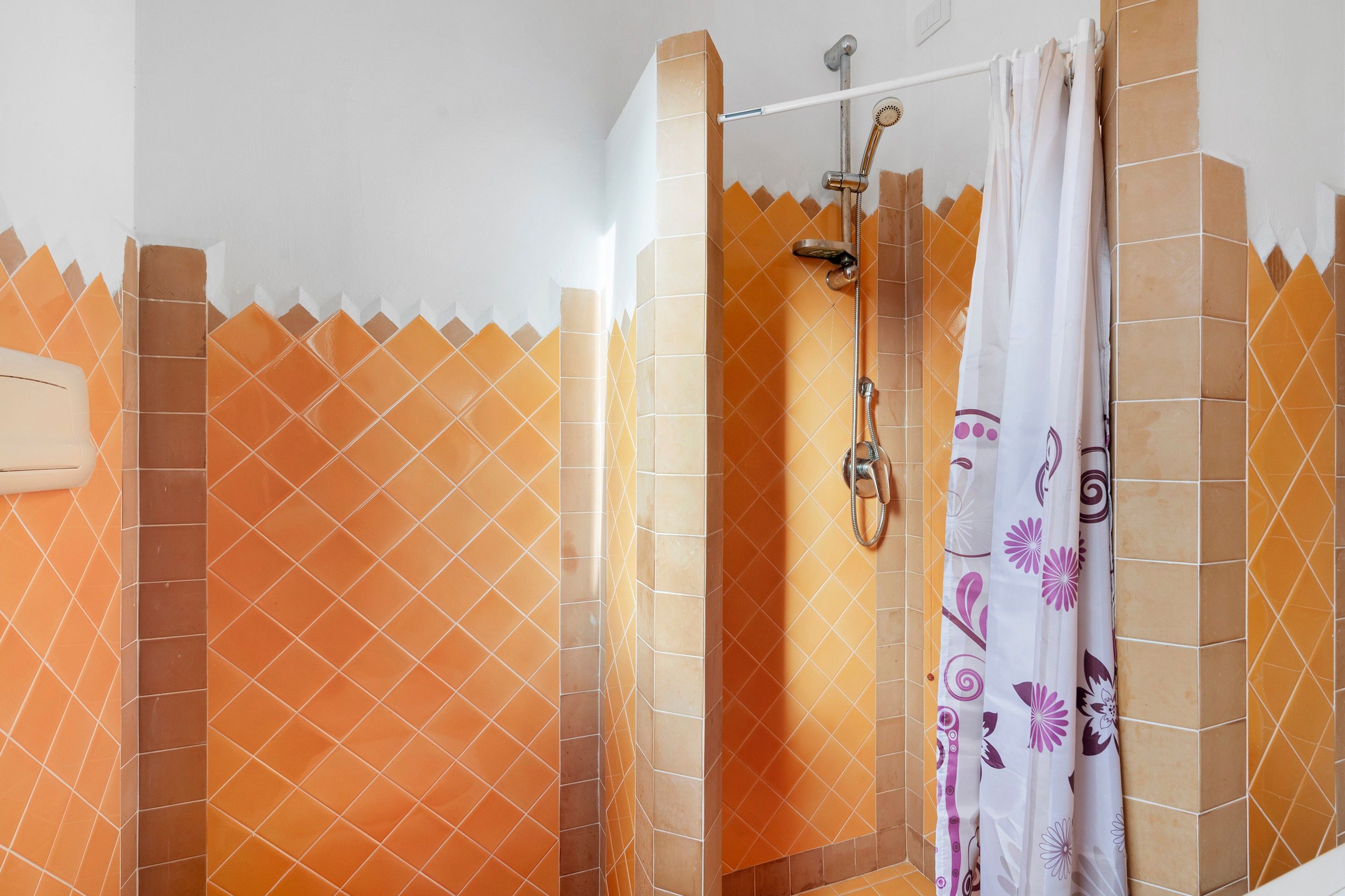 A shower area with a glass door, a handheld showerhead, and a curtain with floral patterns.