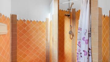 A shower area with a glass door, a handheld showerhead, and a curtain with floral patterns.