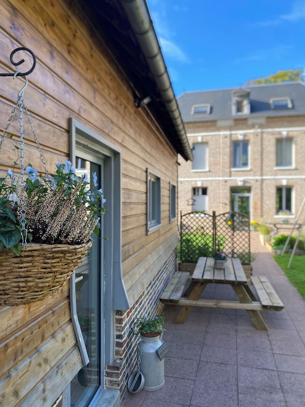 A wooden building with a hanging flower basket, a metal trash can, and a wooden bench.