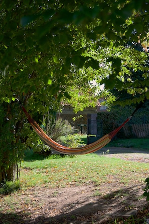 A hammock under a tree in a grassy area with a brick wall and a wooden fence in the background.