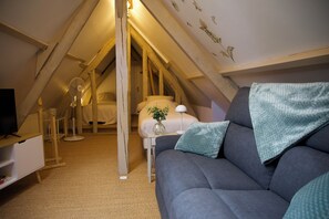 A cozy attic bedroom with a gray sofa, a bedside table with a lamp, and a fan.