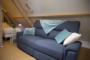Ein Zimmer mit grauem Sofa, einem kleinen Tisch mit Lampe und einem Bett.
