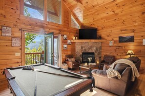 Ein gemütliches Cabin-Interieur mit Billardtisch, Ledersofas, Kamin und einem schönen Blick durch die offene Tür.