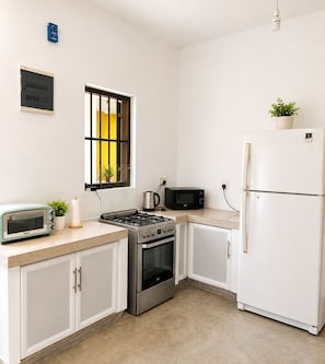 Une cuisine compacte équipée d’une cuisinière à gaz, d’un four à micro-ondes, d’un grille-pain et d’un réfrigérateur blanc.