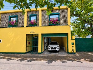 Un immeuble de deux étages avec une façade jaune, une voiture garée dans l’allée et une enseigne sur laquelle on peut lire « VILLA NEFERTUM ».