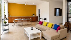 Un salon moderne avec un canapé beige, une table basse blanche et un coin repas comprenant une table et des chaises en verre.