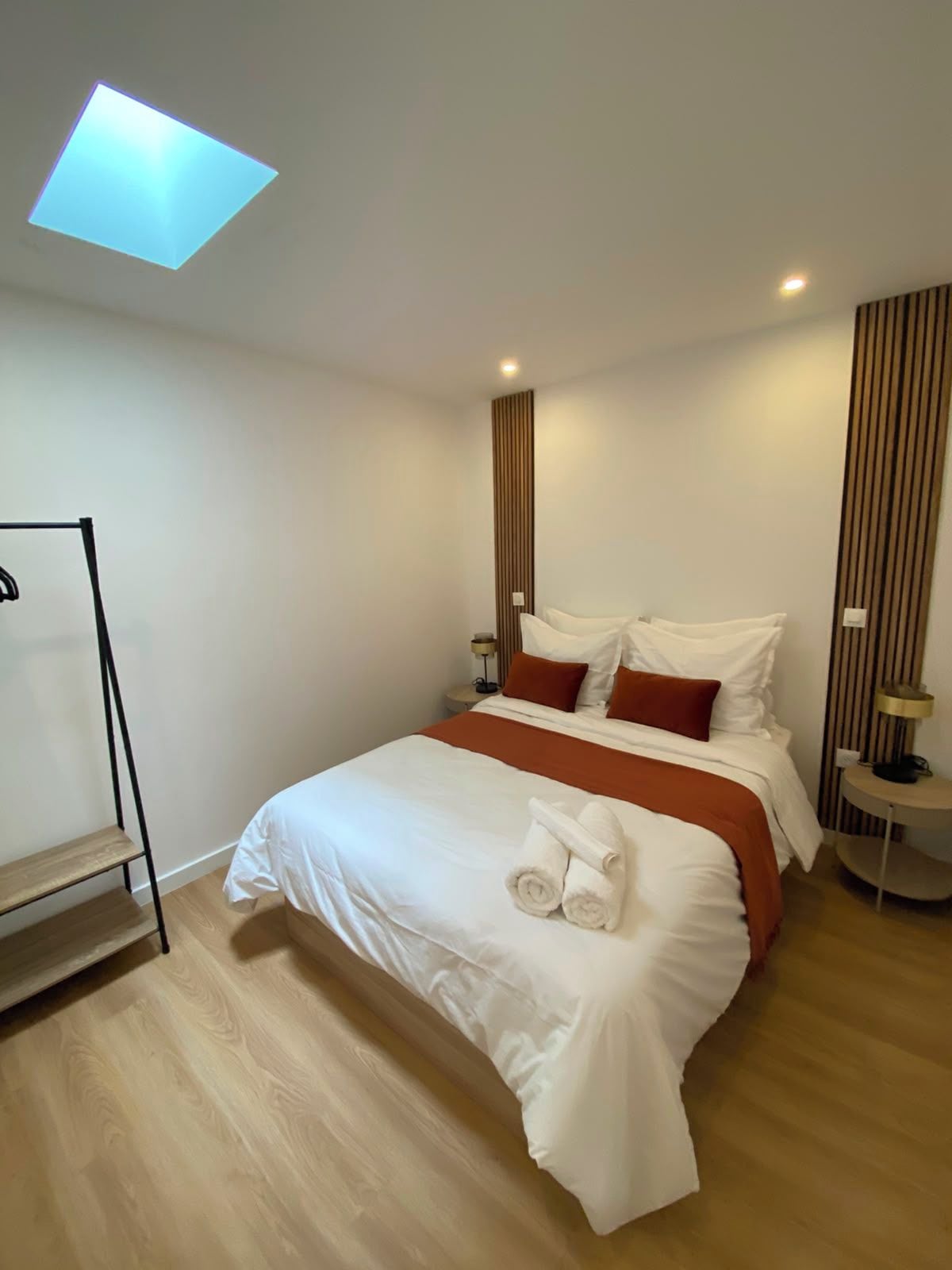 A modern hotel room with a neatly made bed, a standing shelf, and a skylight.