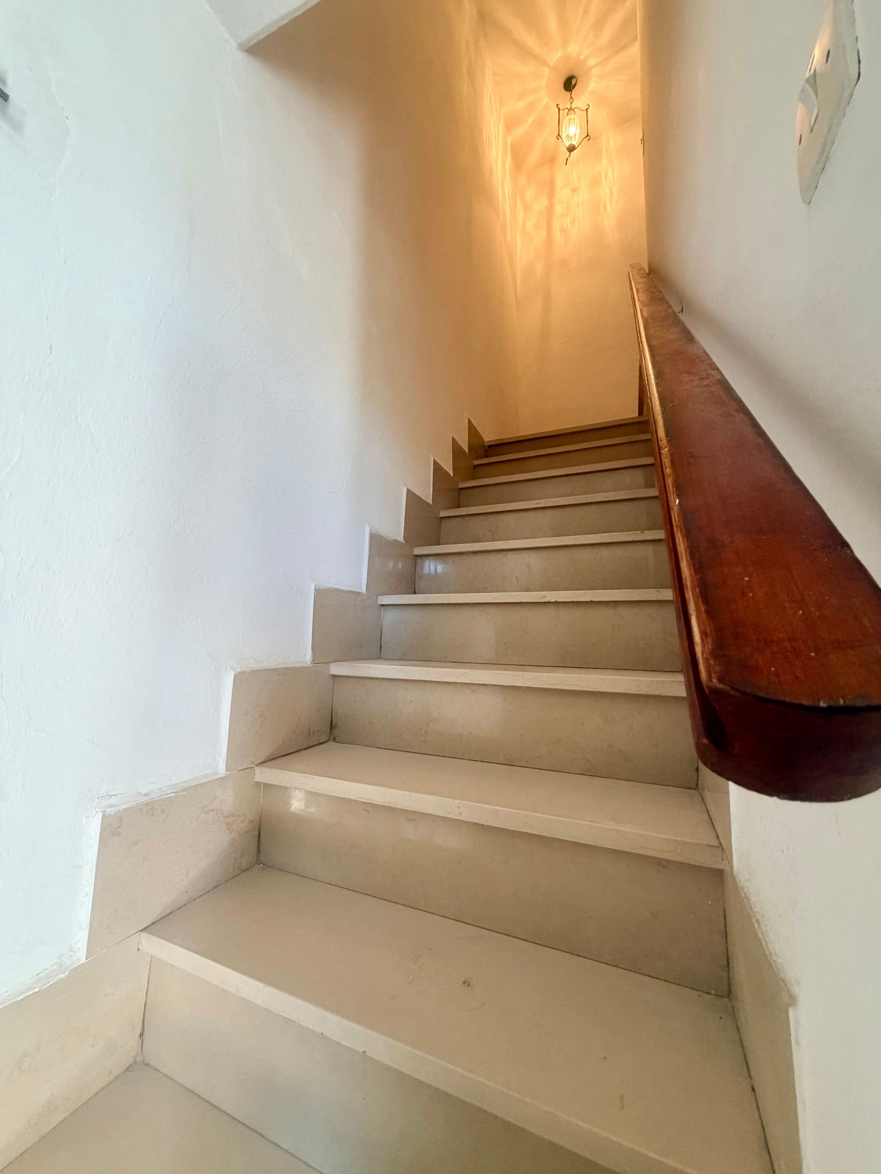 A staircase with a wooden handrail leading to a landing with a wall-mounted light fixture.