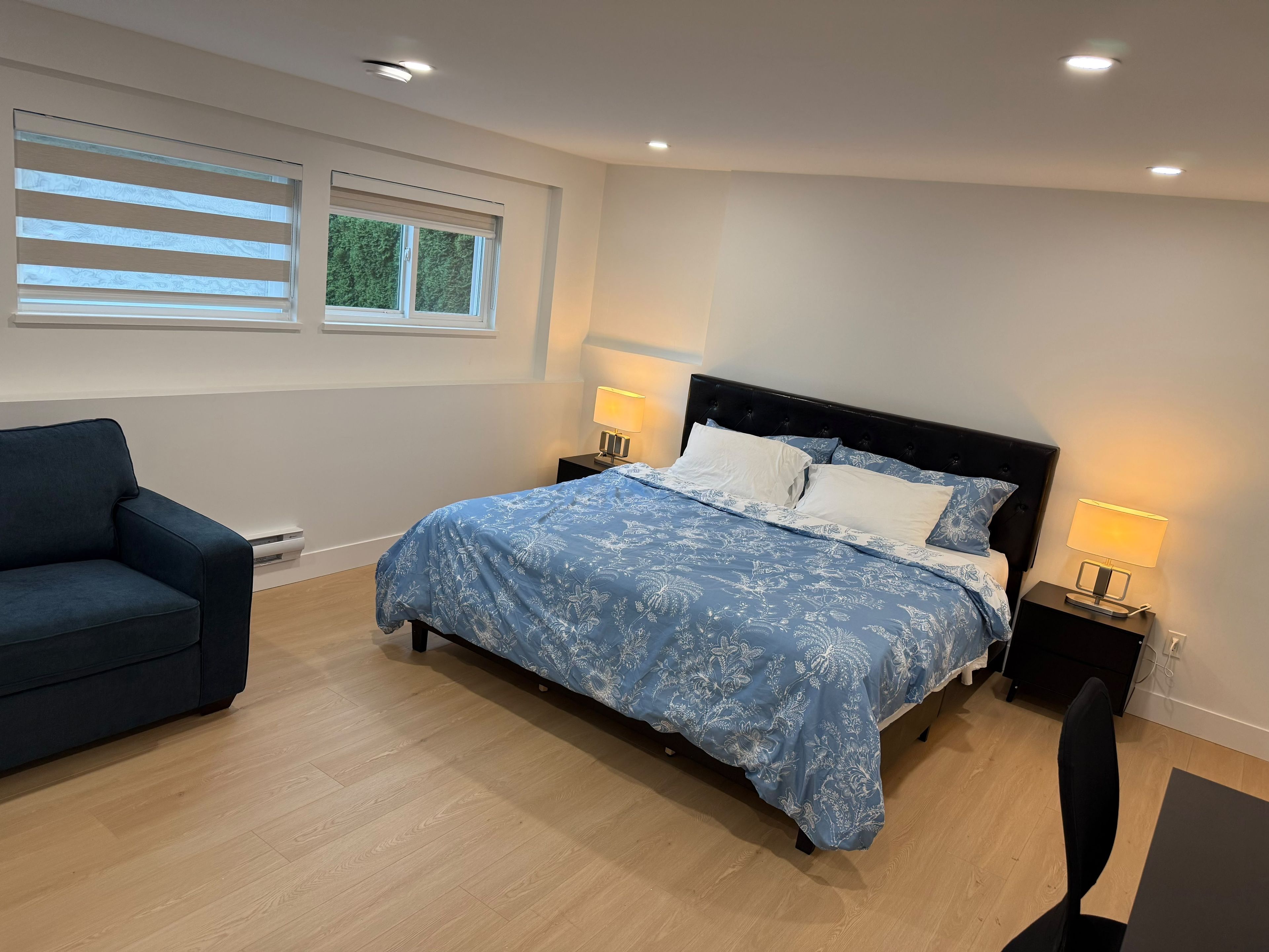 A bedroom with a bed, bedside lamps, a chair, and a window with blinds.