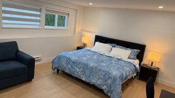 A bedroom with a bed, bedside lamps, a chair, and a window with blinds.