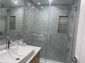 Een moderne badkamer met een douchecabine van glas, een witte wastafel en een spiegel.