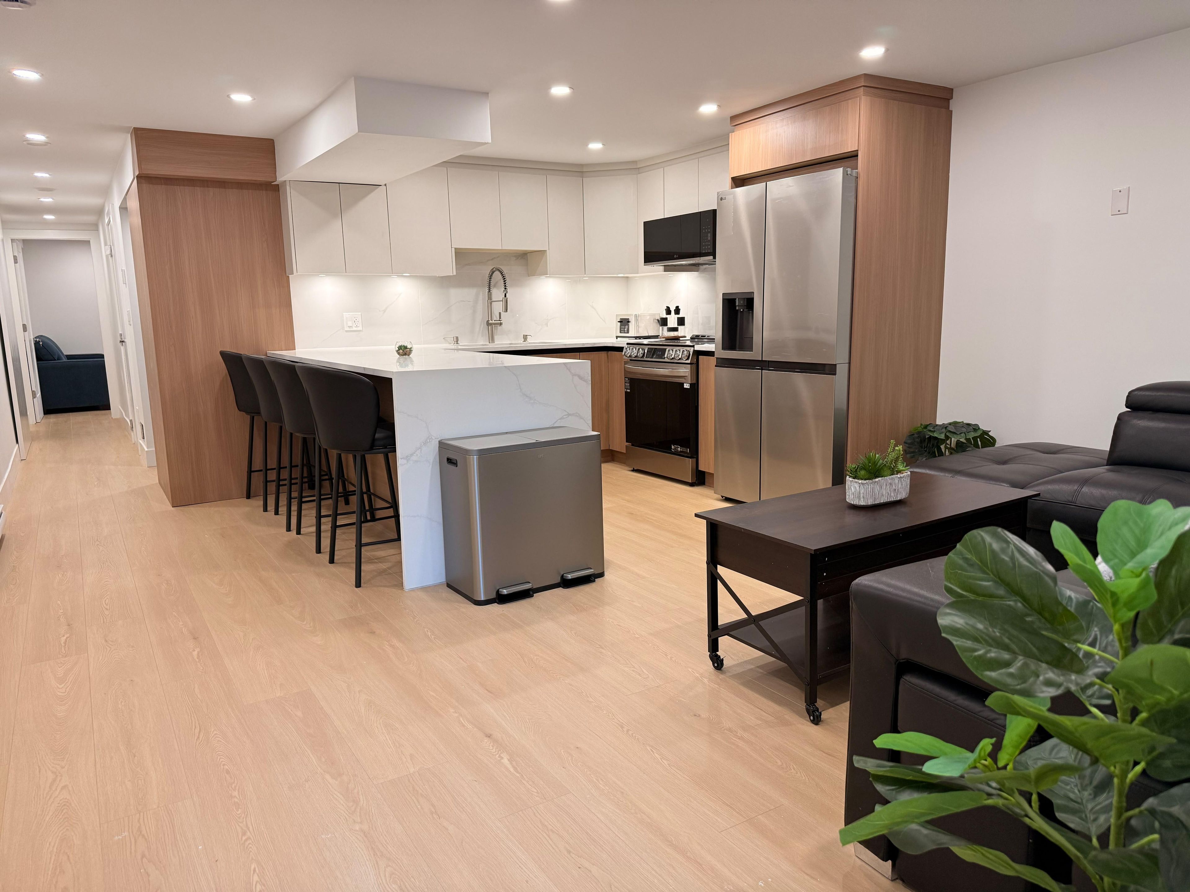 A modern kitchen with a central island, stainless steel appliances, and a seating area with a dark sofa and a small table.