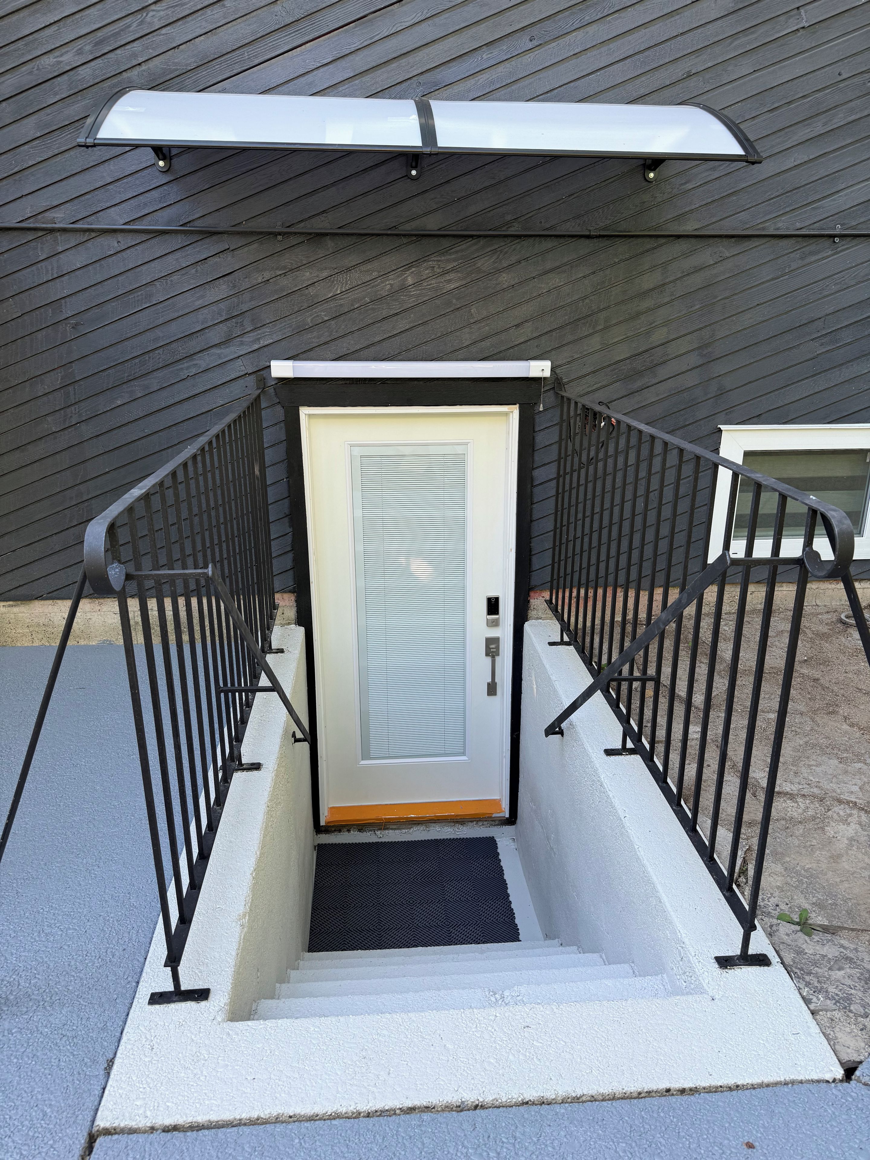 A staircase with a metal railing leading to a door with a window, against a dark wooden wall.