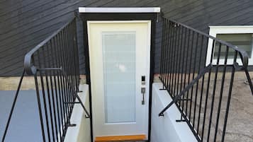 A staircase with a metal railing leading to a door with a window, against a dark wooden wall.