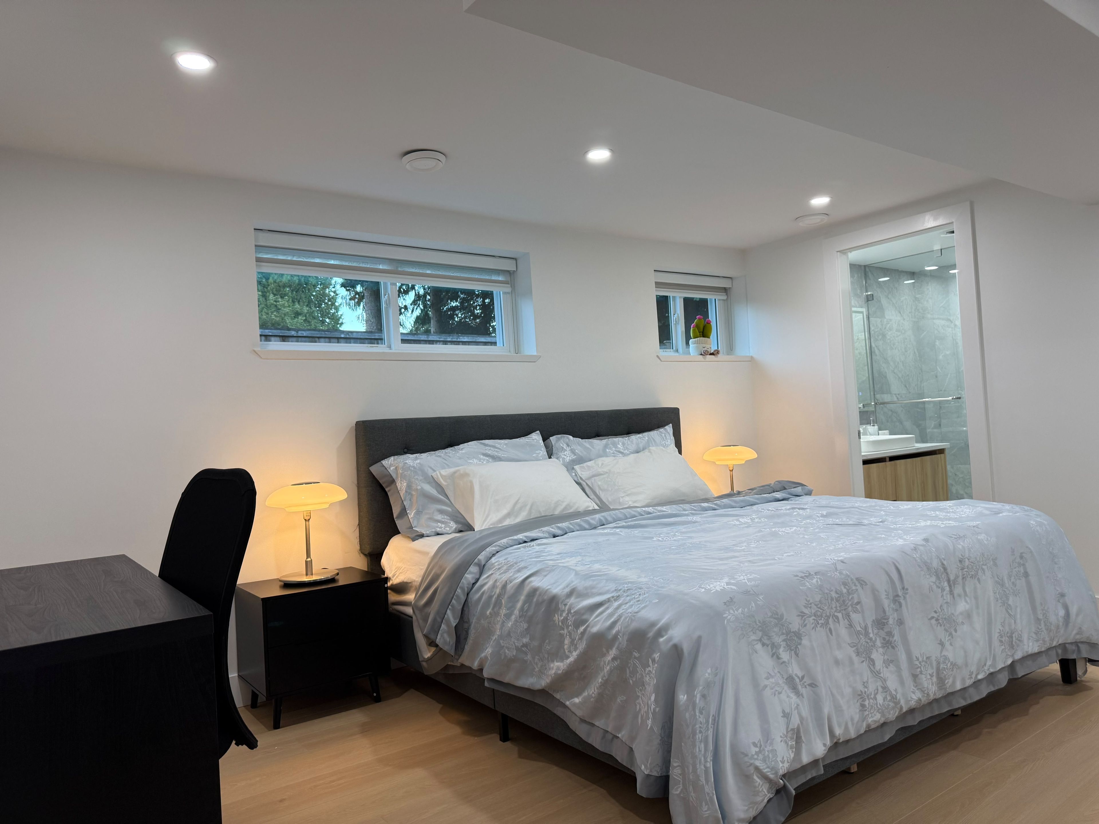 Ein modernes Schlafzimmer mit einem Bett, Nachttischen, einem Schreibtisch und einem Fenster.