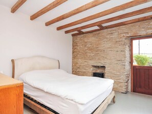 Ein Schlafzimmer mit einem Bett, Holzbalken, einer Steinwand und einer Tür.