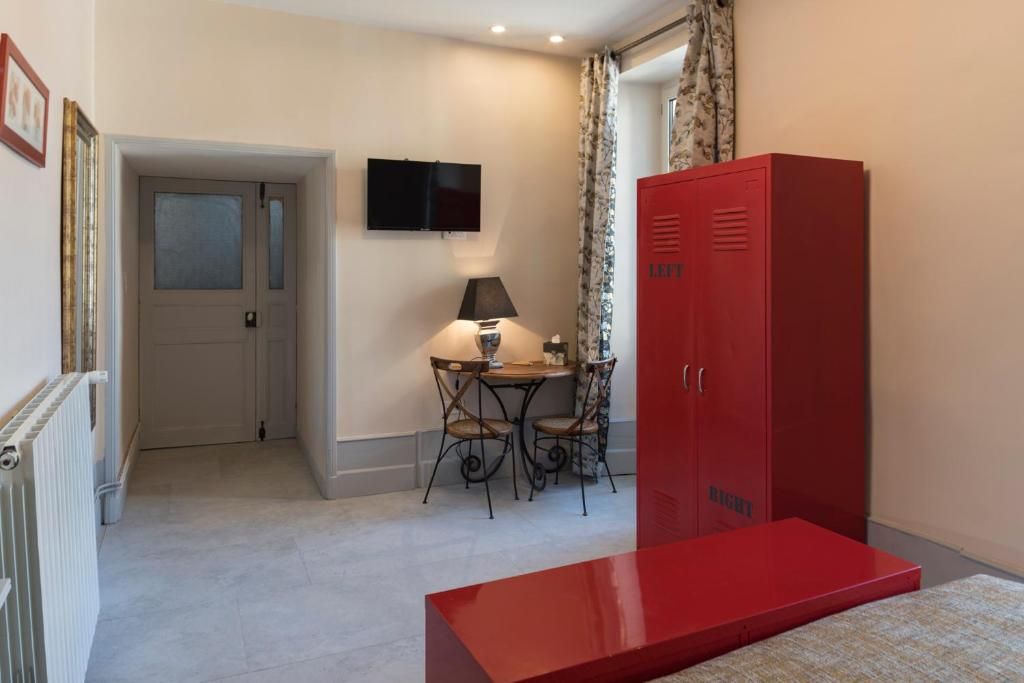A room with a red cabinet, a television on the wall, a table with chairs, and a door leading to another room.