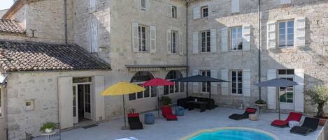 A courtyard with a swimming pool, outdoor seating, and a stone building.