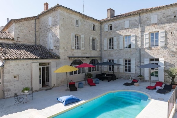 A courtyard with a swimming pool, outdoor seating, and a stone building.