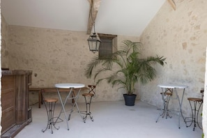 A rustic room with a high ceiling, a wooden cabinet, a potted palm tree, and three metal-framed tables with chairs.