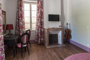 A room with a fireplace, a television mounted on the wall, a violin, and a dining area with chairs and a table.