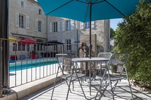 Ein Sitzbereich im Freien mit Blick auf einen Pool, Metallstühle und einem blauen Sonnenschirm.