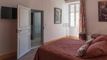 Una camera da letto con un letto, una porta che dà su un'altra stanza, una finestra con tende e un quadro appeso al muro.