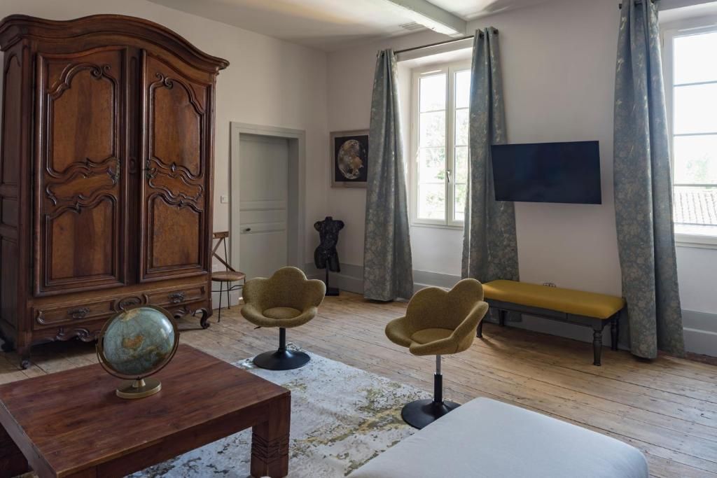Una habitación con un armario de madera, dos sillones, un banco, un globo en una mesa y un televisor montado en la pared.