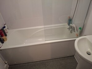 Un baño con bañera, lavamanos y artículos de aseo a un lado.