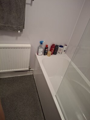 Un baño con una bañera, un perchero para toallas y un estante con diversos artículos de aseo.