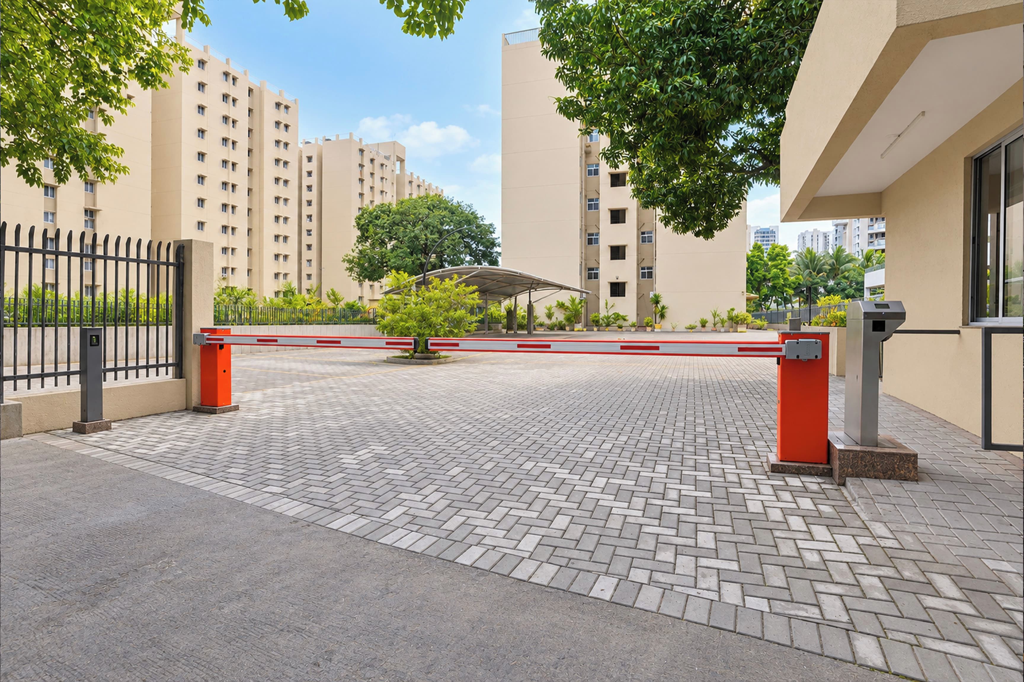 Una entrada cerrada a un área residencial con un camino pavimentado, una reja metálica y un árbol en el centro.