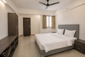 A bedroom with a bed, a wardrobe, a ceiling fan, and a window with curtains. - Townhouse Nanded City (Pune)