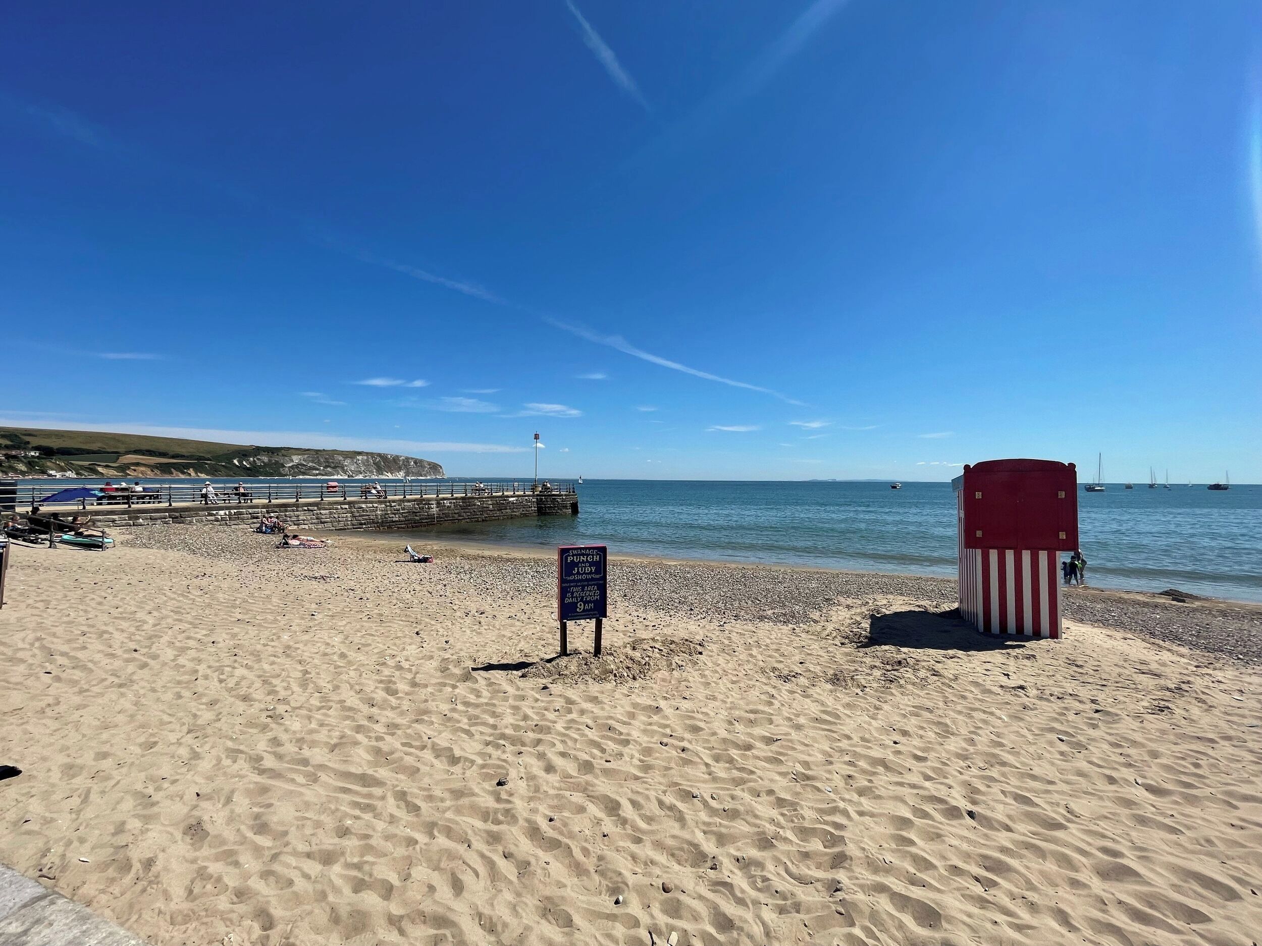 Una playa con una torre de salvavidas, un muelle y un cartel que indica la zona vigilada.