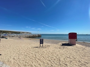 Una playa con una torre de salvavidas, un muelle y un cartel que indica la zona vigilada.