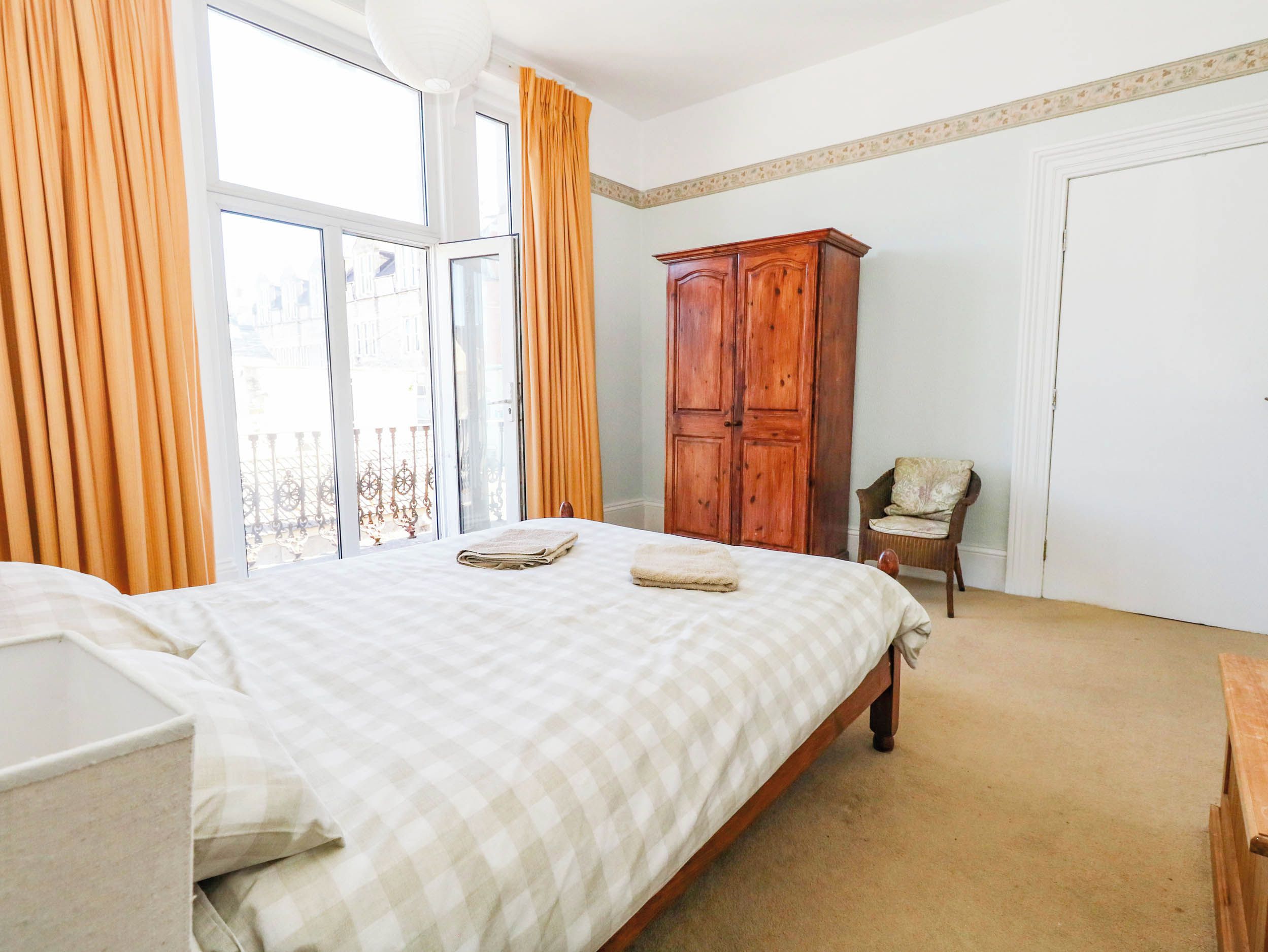 Un dormitorio con una cama, un armario de madera, una silla y un ventanal con cortinas.