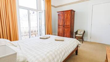 Un dormitorio con una cama, un armario de madera, una silla y un ventanal con cortinas.