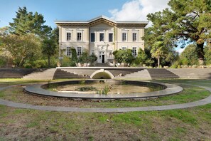 Un grand bâtiment imposant, doté d’une façade symétrique, d’une entrée centrale et d’une fontaine circulaire en premier plan.