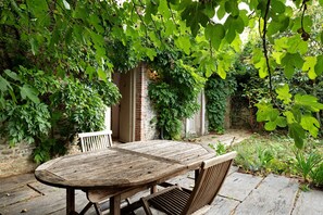A rustic wooden table and chairs set outdoors, surrounded by lush greenery and a brick wall. - Apartment 'Gîte La Rosa - Domaine Les Bois De' with Shared Pool, Shared Terrace and Wi-Fi (Sixt-sur-Aff)
