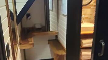 Um corredor estreito com piso de madeira, um pequeno degrau dando acesso a um nível mais alto, e uma porta à direita.