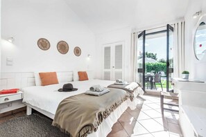 A modern bedroom with a large bed, a bedside table, a nightstand, and a view of the outdoors through a sliding glass door. - Villa Levante - Two Bedroom Villa, Sleeps 4 (Albufeira)