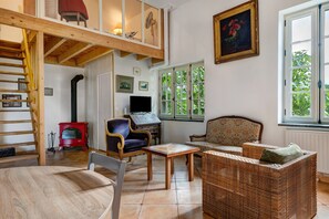 A cozy living room with a high wooden ceiling, a red wood-burning stove, a television, and a comfortable seating area with a sofa and chairs. - Gîte 'Du Bois' with shared pool (Sixt-sur-Aff)
