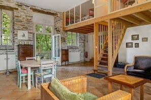 Ein geräumiger Innenraum mit hoher Decke, Steinwänden, einer Holztreppe und einer Essecke mit Tisch und Stühlen.
